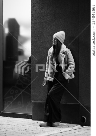 Urban elegance captured at dusk as a woman leans against a wall, exuding style and confidence in a trendy neighborhood, showcasing modern fashion in monochrome Urban elegance captured at dusk as a woman leans against a wall, exuding style and confidence in a trendy neighborhood, showcasing modern fashion in monochrome 124842665