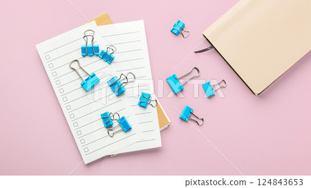 Blue binder clips on checklist paper with notebook on pink background Blue binder clips on checklist paper with notebook on pink background 124843653