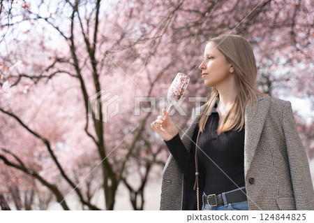 Stylish woman with champagne glass filled with blossoms in blooming park during spring in Prague 124844825