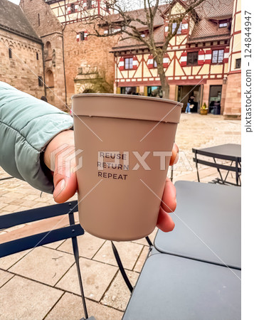 Hand Holding Reusable Coffee Cup Outdoors, Historic Town Setting, Sustainability Concept. High quality photo Hand Holding Reusable Coffee Cup Outdoors, Historic Town Setting, Sustainability Concept. High quality photo 124844947