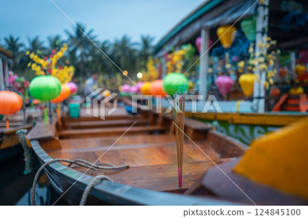 Incense burns on wooden boat in Asian river surrounded by colorful lanterns creating spiritual calm and cultural charm, Smoking ritual floats on tropical waterway, peace and tradition 124845100