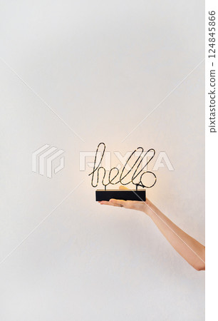 A woman's hand gently holds a decorative 'hello' sign with warm LED lights, creating a welcoming and minimalist scene A woman's hand gently holds a decorative 'hello' sign with warm LED lights, creating a welcoming and minimalist scene 124845866