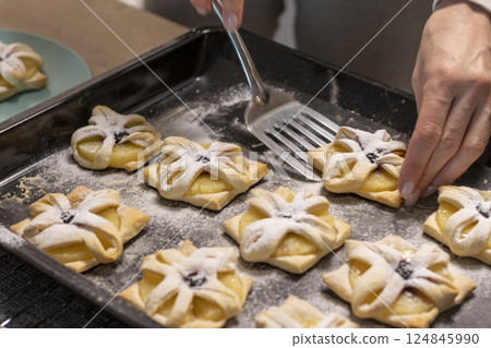 A woman pick the fruit puff pastries with spatula from baking tray and places them on ceramic plate 124845990