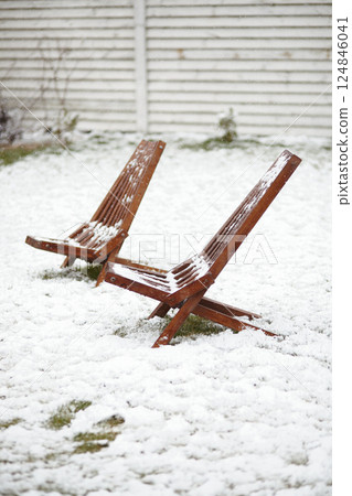Snow-covered wooden chairs standing in a grassy backyard during a spring snowfall. A serene wintery view representing climate anomalies and return of freezing temperatures. Snow-covered wooden chairs standing in a grassy backyard during a spring snowfall. A serene wintery view representing climate anomalies and return of freezing temperatures. 124846041