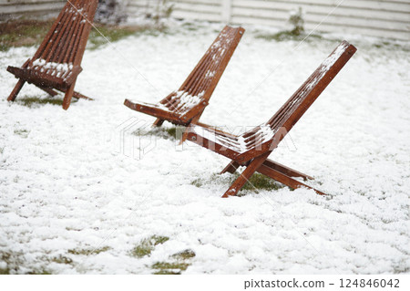 Three wooden lounge chairs in a backyard under spring snowfall, symbolizing unusual climate conditions Three wooden lounge chairs in a backyard under spring snowfall, symbolizing unusual climate conditions 124846042