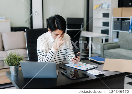 Serious young man sit at workplace desk in office use calculator calculates monthly expenses, taxes, personal budget management concept 124846470