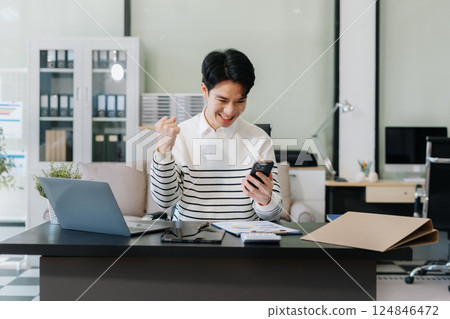 Successful business man, excited young man Keeping up arms and showing positive emotions, happy working in modern office on computer. 124846472