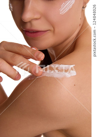 Cropped photo of young woman applying protecting cream on bare shoulder against white studio background. Soft and healthy skin. 124848026
