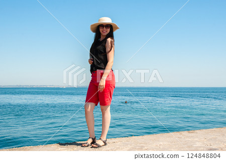 Elegant woman in sun hat enjoying a day by the sea. Happy summer days, travel and vacation concept 124848804