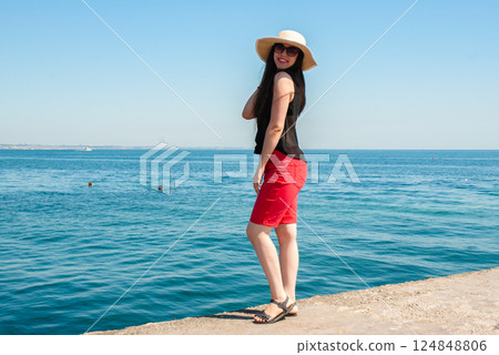 Woman enjoying a sunny day by the sea in summer attire. Happy summer days, travel and vacation concept Woman enjoying a sunny day by the sea in summer attire. Happy summer days, travel and vacation concept 124848806
