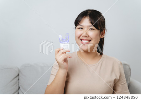 The woman is whitening her teeth with a teeth whitening device by herself The woman is whitening her teeth with a teeth whitening device by herself 124848850