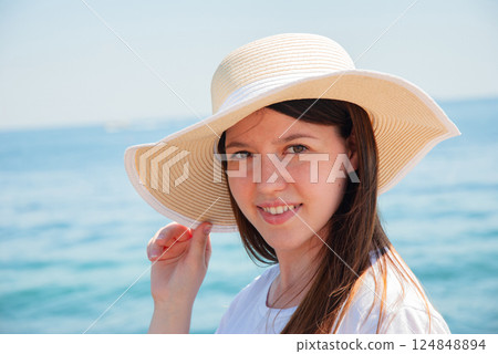 Summer beach portrait of a young woman with sun hat by the ocean. Happy summer days, travel and vacation concept 124848894
