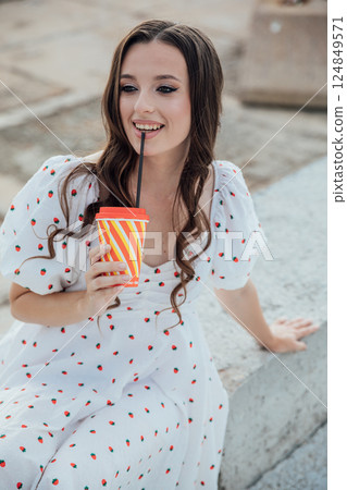 Beautiful slim fashionable brunette woman in summer dress sitting with a straw drink 124849571