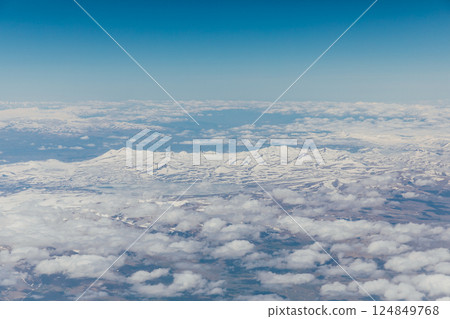 Beautiful landscape on snowy mountains with clouds from the window of an airplane 124849768