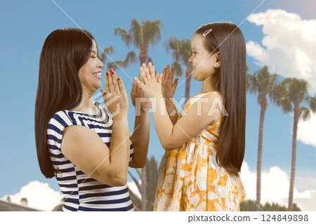 Mother and her little girl play clapping game outdoors. Blue sky and palms background. 124849898