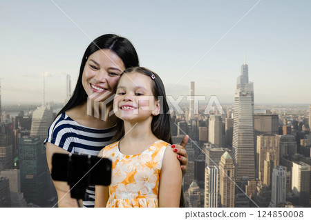 Brunette woman and little girl are making a selfie shot on smartphone. Urban cityscape background. Brunette woman and little girl are making a selfie shot on smartphone. Urban cityscape background. 124850008
