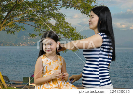 Portrait of brunette woman is combing a little girl outdoors. Sea resort vacation background. 124850025