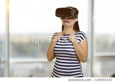 Scared woman in vr headset standing indoors. Blurred windows background. Scared woman in vr headset standing indoors. Blurred windows background. 124850131