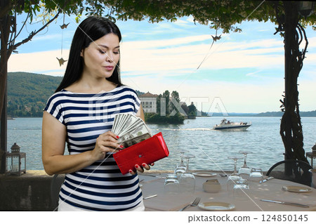 Asian woman is getting dollars from her red wallet on vacation. Summer resort background. Asian woman is getting dollars from her red wallet on vacation. Summer resort background. 124850145