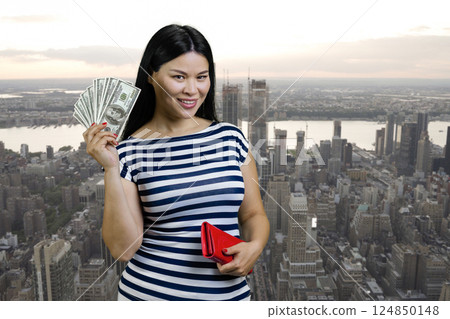 Young asian woman is holding fan of dollars from a red wallet. Urban cityscape background. Young asian woman is holding fan of dollars from a red wallet. Urban cityscape background. 124850148
