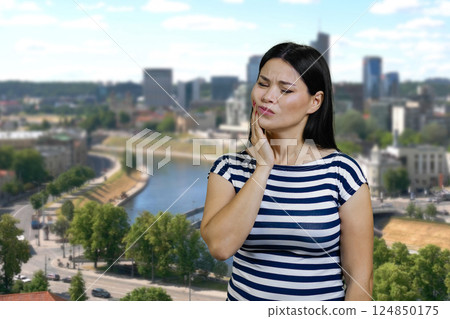 Young asian woman touching her cheek because of toothache. Urban cityscape background. 124850175