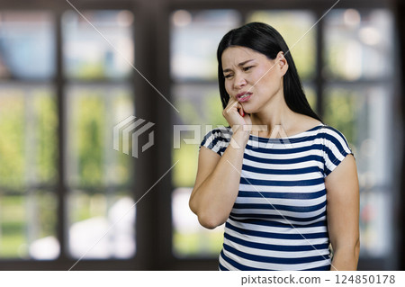 Portrait of an asian woman suffering from toothache indoors. Blurred checkered windows background. 124850178