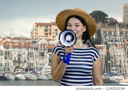 Young asian woman with megaphone against yacht harbour background. Female tourist guide with loudspeker. 124850194