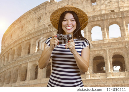 Young asian female tourist wearing straw hat. Holding a vintage photo camera. Rome Coliseum background. 124850211