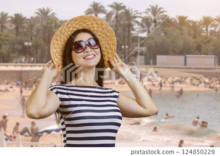 Happy young woman with straw hat standing outdoors. Beach resort background. Happy young woman with straw hat standing outdoors. Beach resort background. 124850229