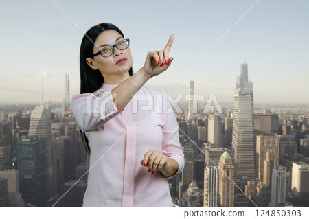 Asian businesswoman is pointing at copy space using invisible virtual screen. Urban cityscape background. 124850303