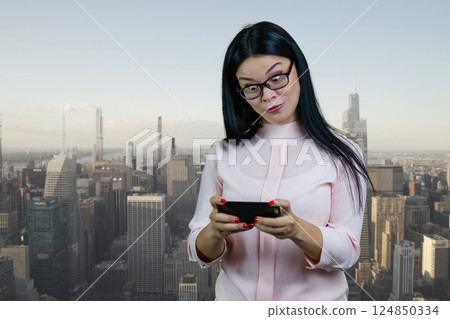 Young asian woman is surprised to see something on her smartphone. Urban cityscape background. 124850334