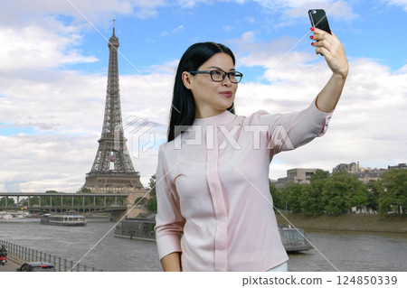 Portrait of a young asian woman taking a selfie on her smartphone. Outdoor Eiffel Tower in Paris on the background. 124850339