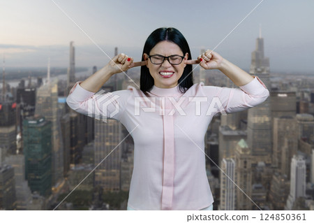 Young asian woman is closing her ears with fingers. Urban cityscape background. Young asian woman is closing her ears with fingers. Urban cityscape background. 124850361