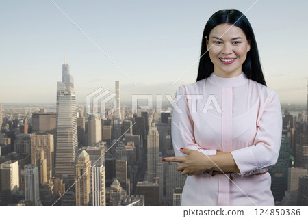 Portrait of a young asian businesswoman with folded arms pointing at copy space. Cityscape with skyscrappers background. Portrait of a young asian businesswoman with folded arms pointing at copy space. Cityscape with skyscrappers background. 124850386