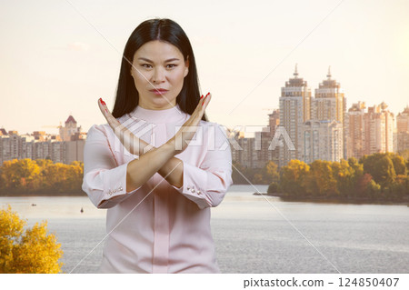 Asian brunette woman holding two arms crossed gesturing no sign. Portrait of young korean busimesswoman rejecting you outdoors. 124850407