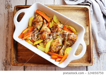 Roasted chicken drumsticks with potatoes and carrots. Chicken legs grilled on a grill pan close-up. Horizontal view from above 124850750