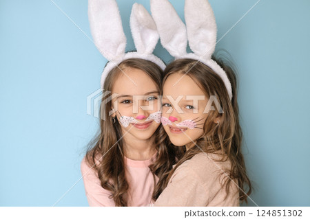 Cute cute girls with painted rabbit faces on their faces and bunny ears on heads are hugging each other and looking sweetly at the camera. Easter Holiday Day 124851302