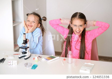Happy children at a school desk in a science school examine liquids and cells of objects under a microscope Happy children at a school desk in a science school examine liquids and cells of objects under a microscope 124851336