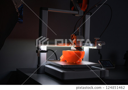 3D Printer Creating Orange Plastic Object on Platform 124851462