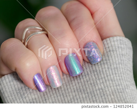 Skittles nails on hand. Colorful shiny manicure with different textures in light purple tones, pink and lilac hue. Closu-up of female hand with multicolored nails on green foliage background. Copy Skittles nails on hand. Colorful shiny manicure with different textures in light purple tones, pink and lilac hue. Closu-up of female hand with multicolored nails on green foliage background. Copy 124852041