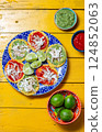 Vibrant chalupas with green and red sauces served on a decorative plate beside limes and bowls of salsa 124852063