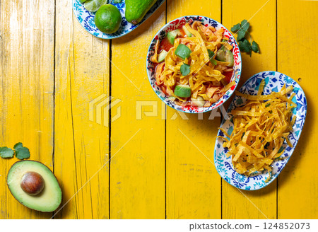 Delicious tortilla fried Aztec soup served with fresh avocado and lime on a vibrant yellow table 124852073