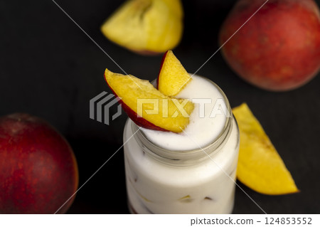 yogurt and peaches cut into pieces on black slate, fermented milk product with peach flavor with the addition of pieces of peach, close up 124853552