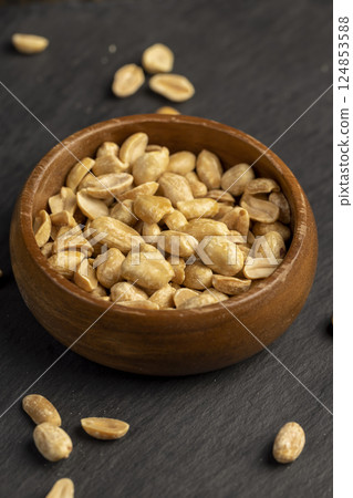 peanuts in a wooden round bowl, crunchy peanuts without shells on a black slate board, close up peanuts in a wooden round bowl, crunchy peanuts without shells on a black slate board, close up 124853588