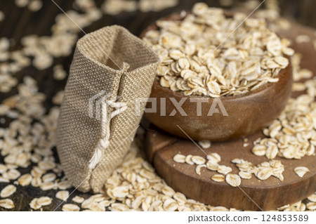 bowl and a linen bag with oatmeal flakes for making porridge, scattered dry cereal flakes from oats, flattened, steamed and dried bowl and a linen bag with oatmeal flakes for making porridge, scattered dry cereal flakes from oats, flattened, steamed and dried 124853589