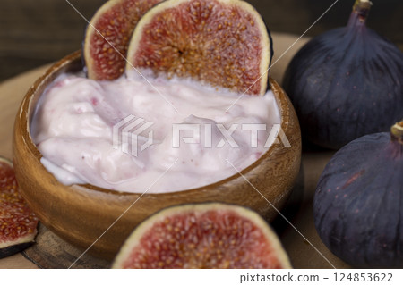 yogurt with fresh figs, fresh pink yogurt with fig flavor in a wooden bowl with red figs cut into pieces, side view 124853622