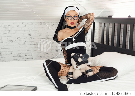 A girl in a sexy nun dress from an adult role-playing sex shop and stockings excitingly poses on a bedroom bed A girl in a sexy nun dress from an adult role-playing sex shop and stockings excitingly poses on a bedroom bed 124853662