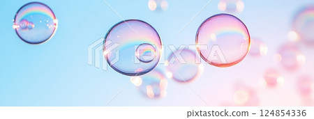 Rainbow soap bubbles are floating on a blue sky background, creating a colorful and dreamy atmosphere with their iridescence and delicate fragility 124854336