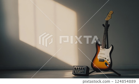 Sunbeams illuminate an electric guitar on a stand next to a portable amplifier, creating a serene atmosphere perfect for music creation or practice 124854889