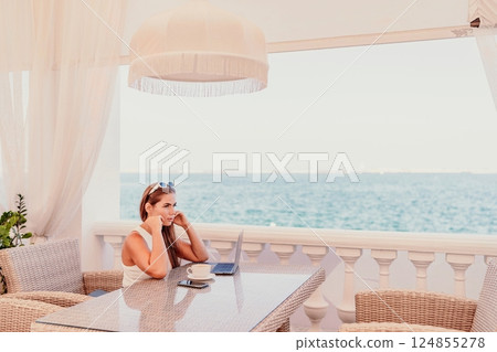 Woman coffee cafe laptop sea. Female freelancer using laptop on coffee break in modern cafe with sea view in the morning Woman coffee cafe laptop sea. Female freelancer using laptop on coffee break in modern cafe with sea view in the morning 124855278